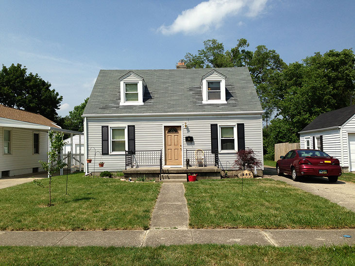 Cape Cod, grey siding, small trees, sidewalk